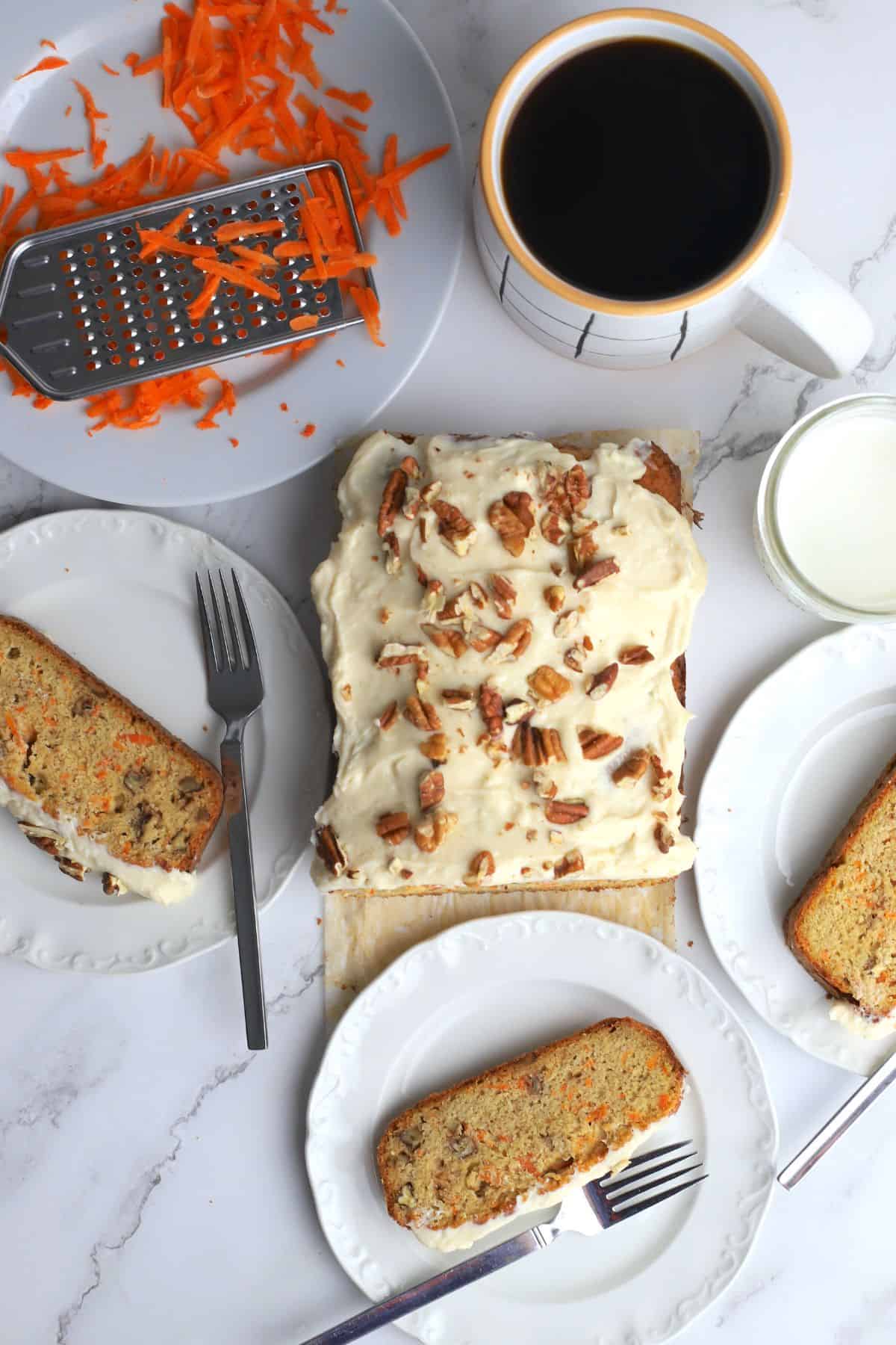 Sugar free carrot cake next to a coffee mug, dessert plates and shredded carrots.