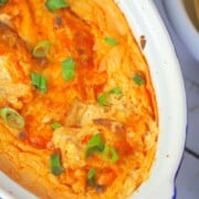 casserole of buffalo dip with bowls of nacho chips pecans and cheese crackers and a tv remote.