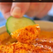 dipping a cucumber slice into the hummus.