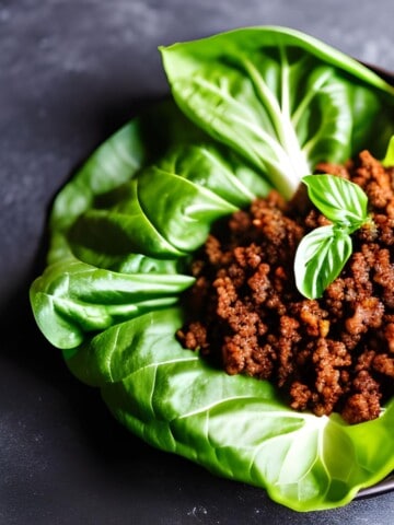 ground meat on a lettuce leaf topped with two basil leaves.