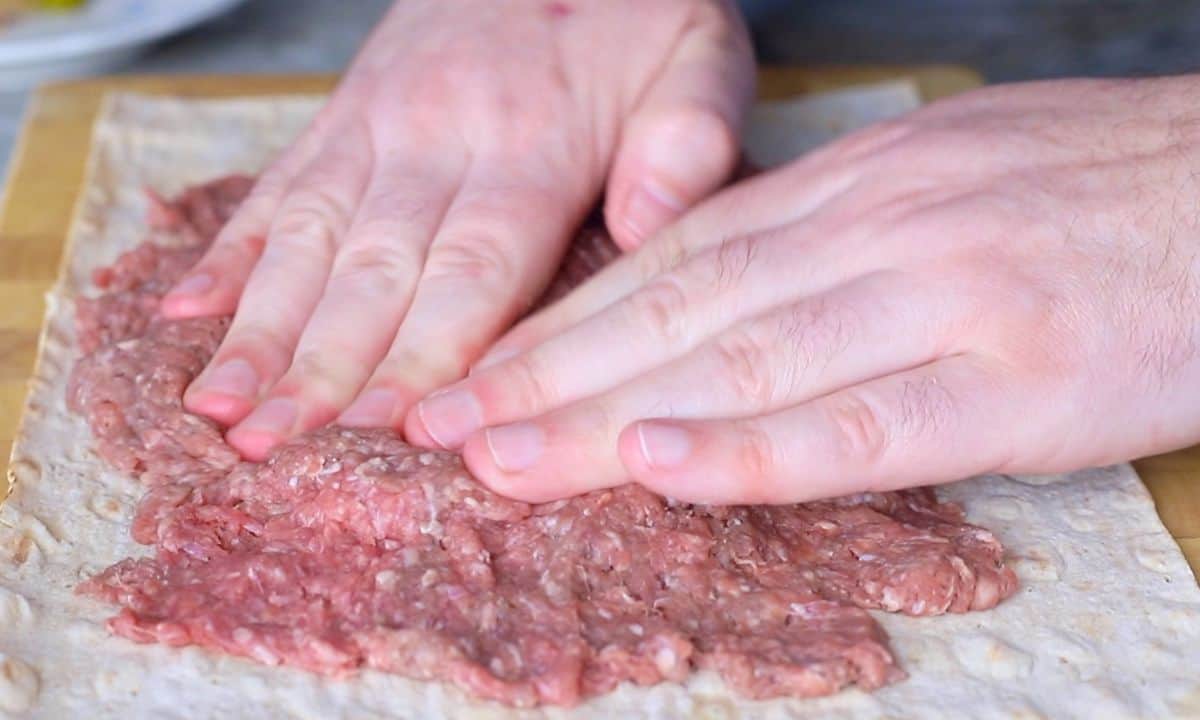 pressing ground meat onto a lavash bread wrap.