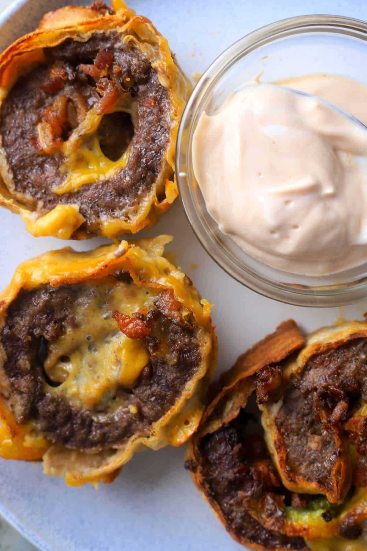 Cheeseburger roll ups on a dish next to a small bowl with dipping sauce.