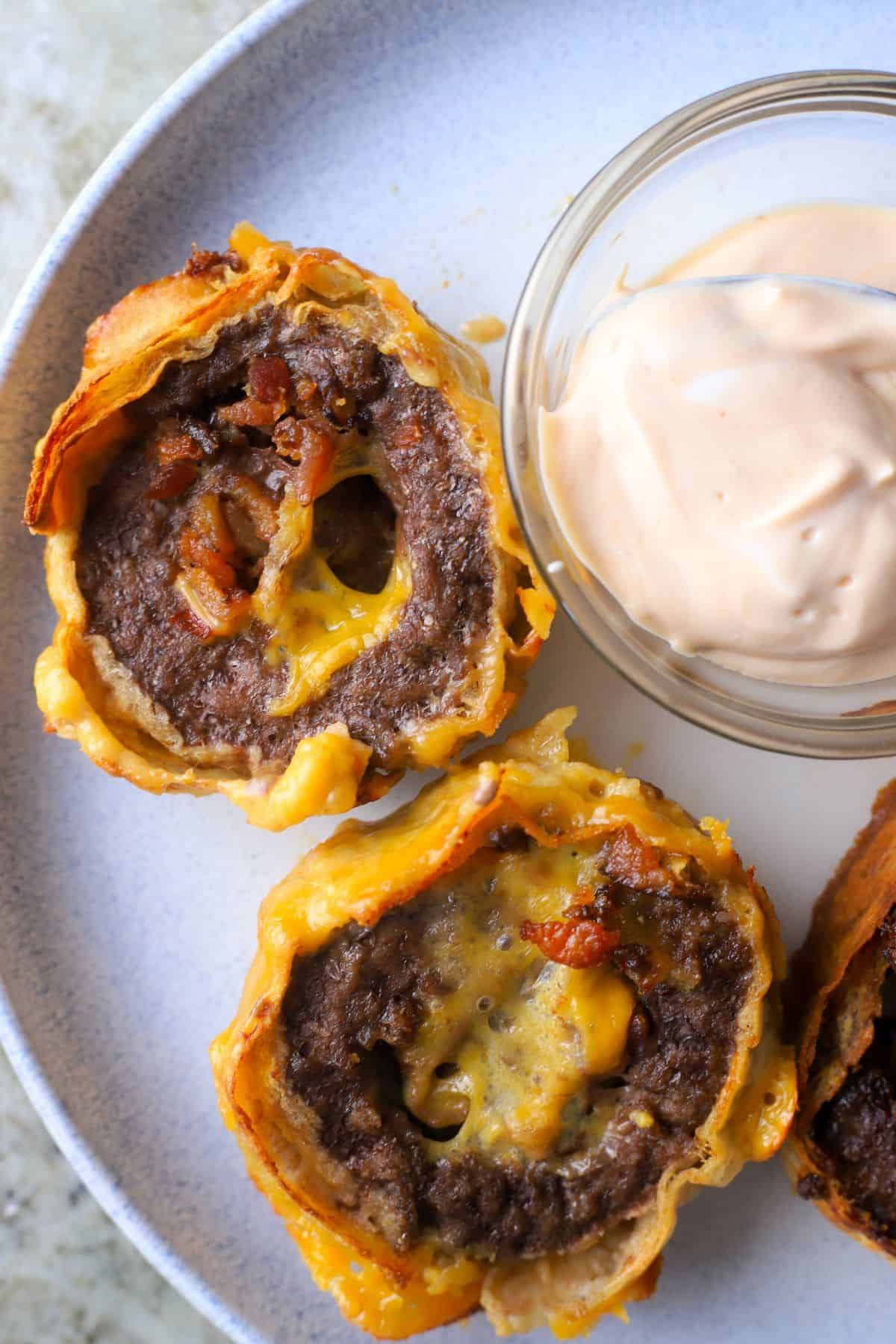 Cheeseburger roll ups on a dish next to a small bowl with dipping sauce.