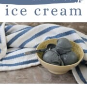 a bowl with blueberry ice cream and a spoon along side a blue and white striped napkin.