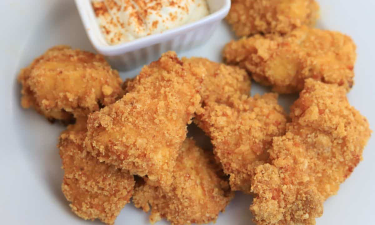 chicken nuggets on a white plate next to a small bowl with dip.