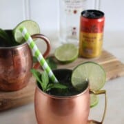 moscow mule in a copper mug with a straw and garnished with mint and a lime.