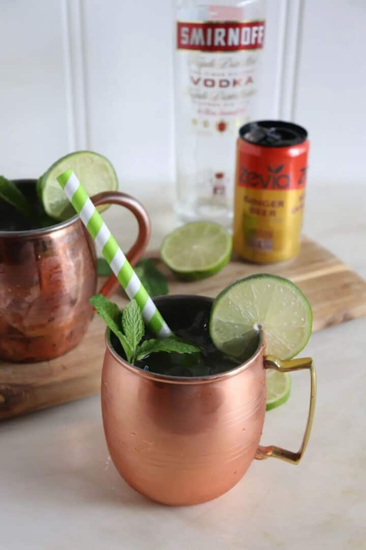 moscow mule in a copper mug with a straw and garnished with mint and a lime.