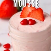 keto strawberry mousse in a small glass jar topped with strawberry slices and two cinnamon hearts.