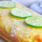 Lime drizzle cake loaf topped with a sprinkle of powdered sugar and 3 lime slices.