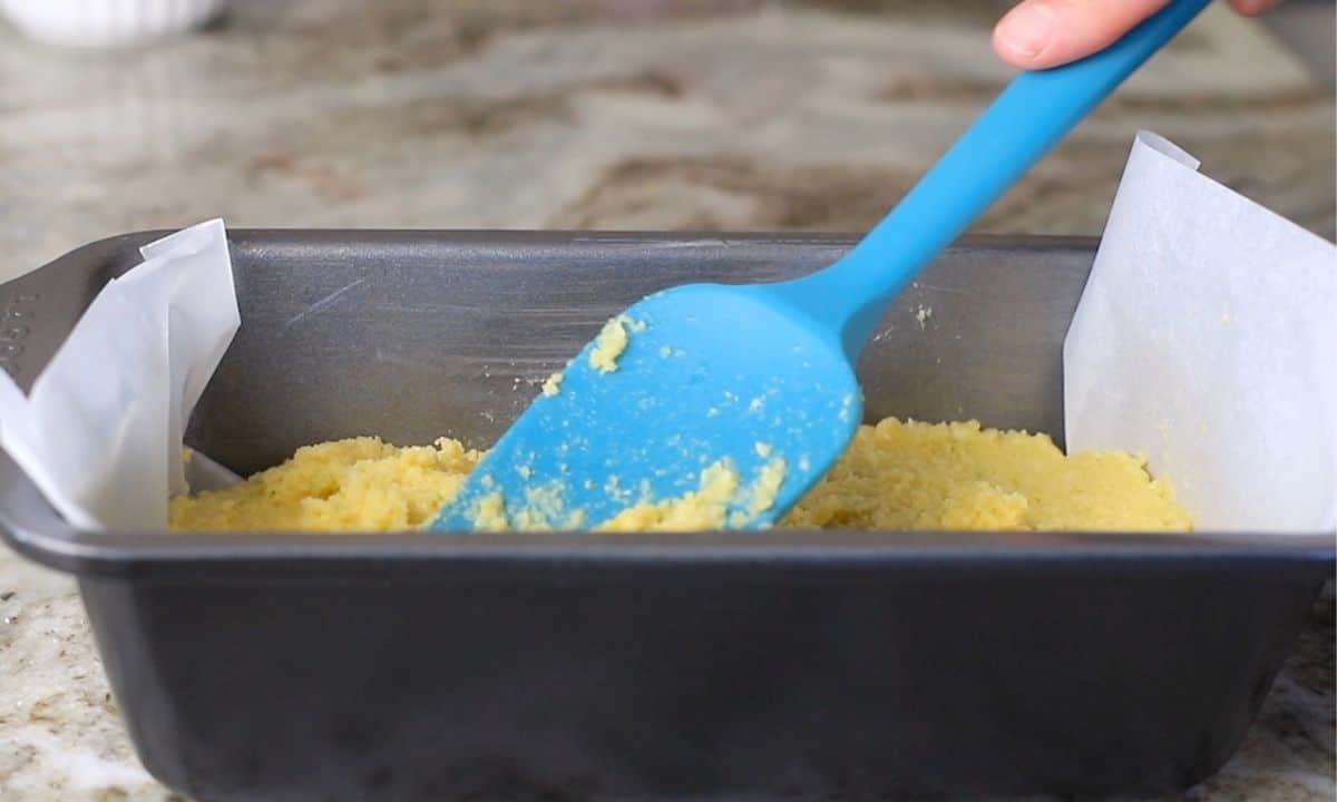 loaf pan with batter and a blue rubber spatula smoothing out the top.