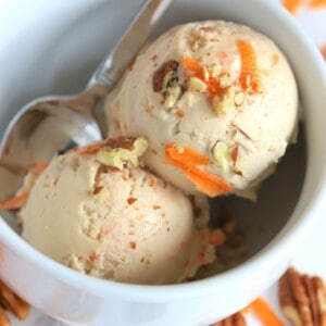 ninja creami carrot cake ice cream in a bowl with a spoon next to carrot shreds and pecans.