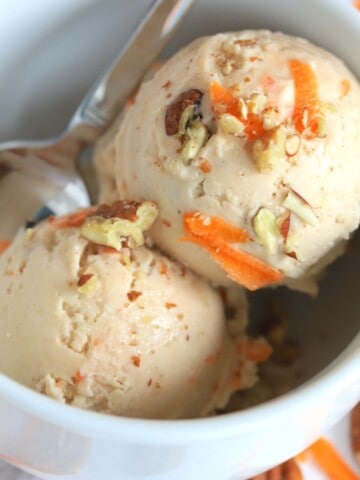 ninja creami carrot cake ice cream in a bowl with a spoon next to carrot shreds and pecans.