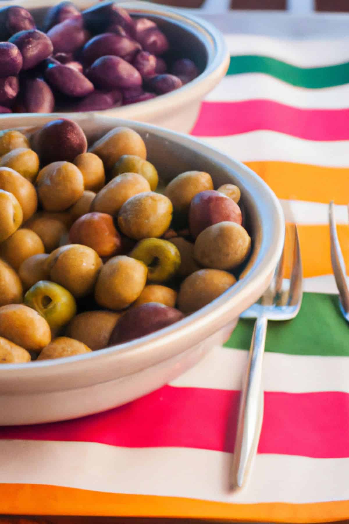 two bowls of olives on a striped tablecloth with a fork.