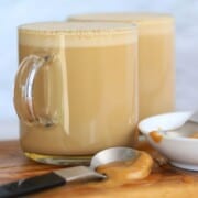 two glass mugs of peanut butter coffee with a spoon full of peanut butter resting in front of them.