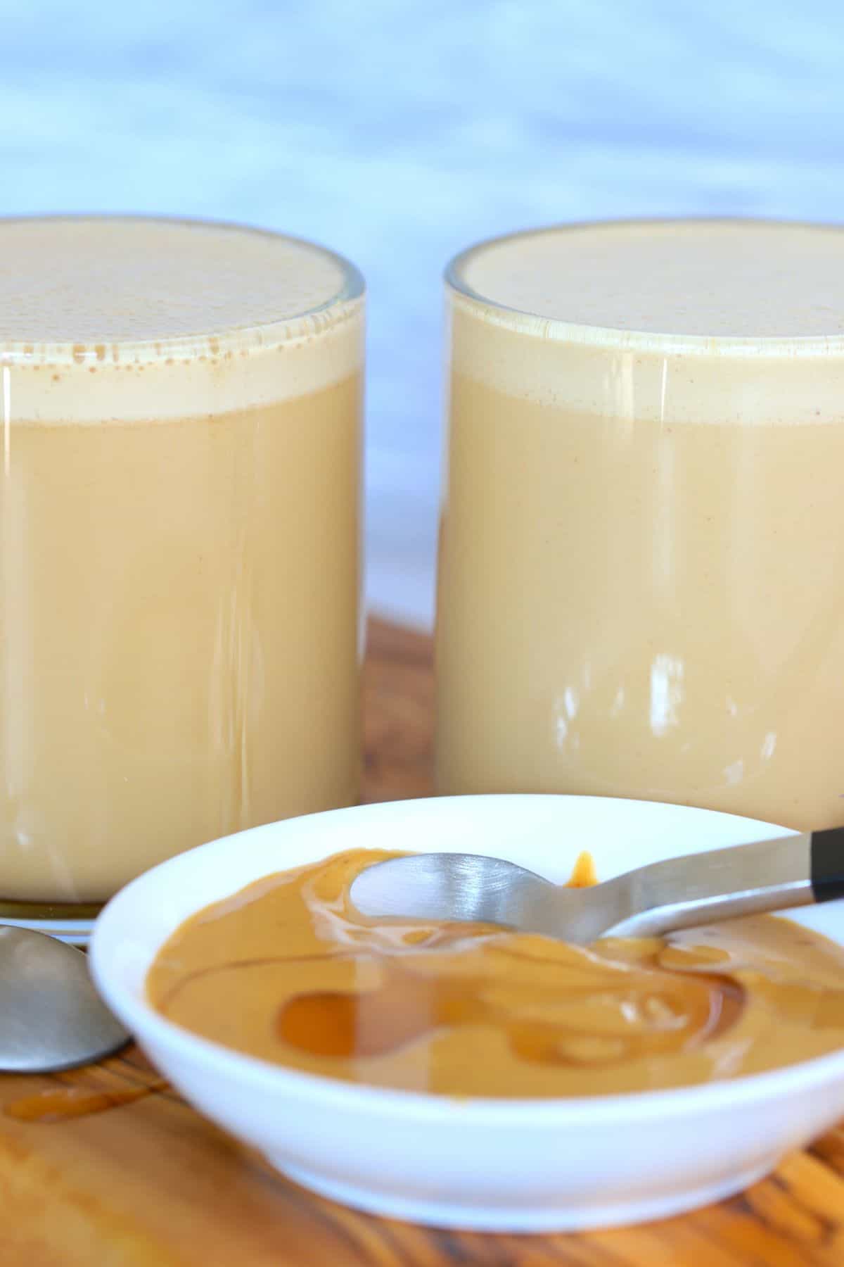 two glass mugs of peanut butter coffee with a small bowl of peanut butter resting in front of them.