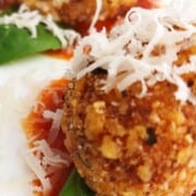 ricotta balls on tomato sauce and a basil leaf on a white plate.