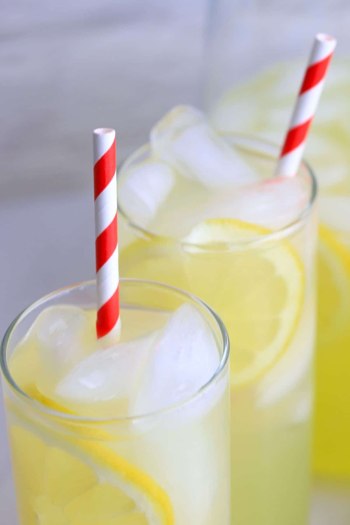 two glasses filled with lemonade next to a half-filled jug.