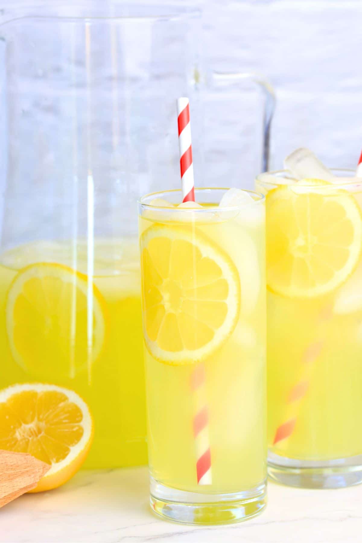 two glasses filled with lemonade next to a half filled jug.