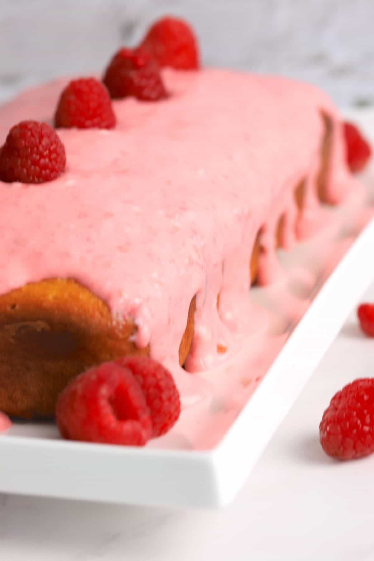 side shot of the cake with the icing dripping down the sides and some raspberries scattered around it.