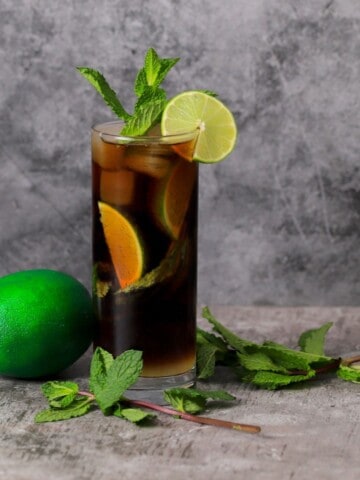 a black mojito in a tall glass garnished with mint and lime with a full lime next to the glass.