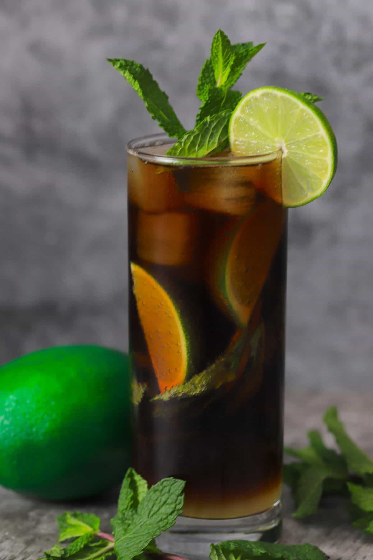 a black mojito in a tall glass garnished with mint and lime with a full lime next to the glass.