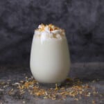coconut milk shake in a stemless wine glass topped with whipped cream and toasted shredded coconut flakes.