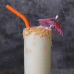 coconut pineapple margarita cocktail garnished with toasted coconut and a cocktail umbrella with an orange straw.
