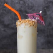 coconut pineapple margarita cocktail garnished with toasted coconut and a cocktail umbrella with an orange straw.
