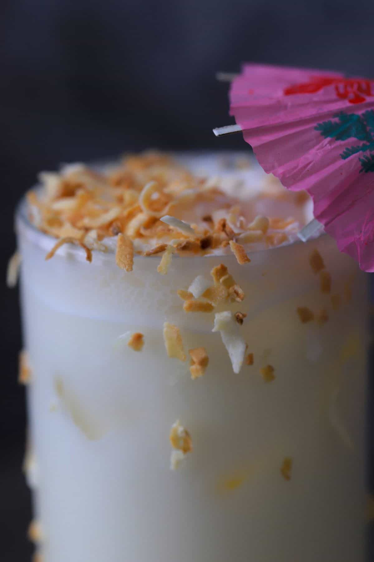 coconut pineapple margarita cocktail garnished with toasted coconut and a cocktail umbrella.