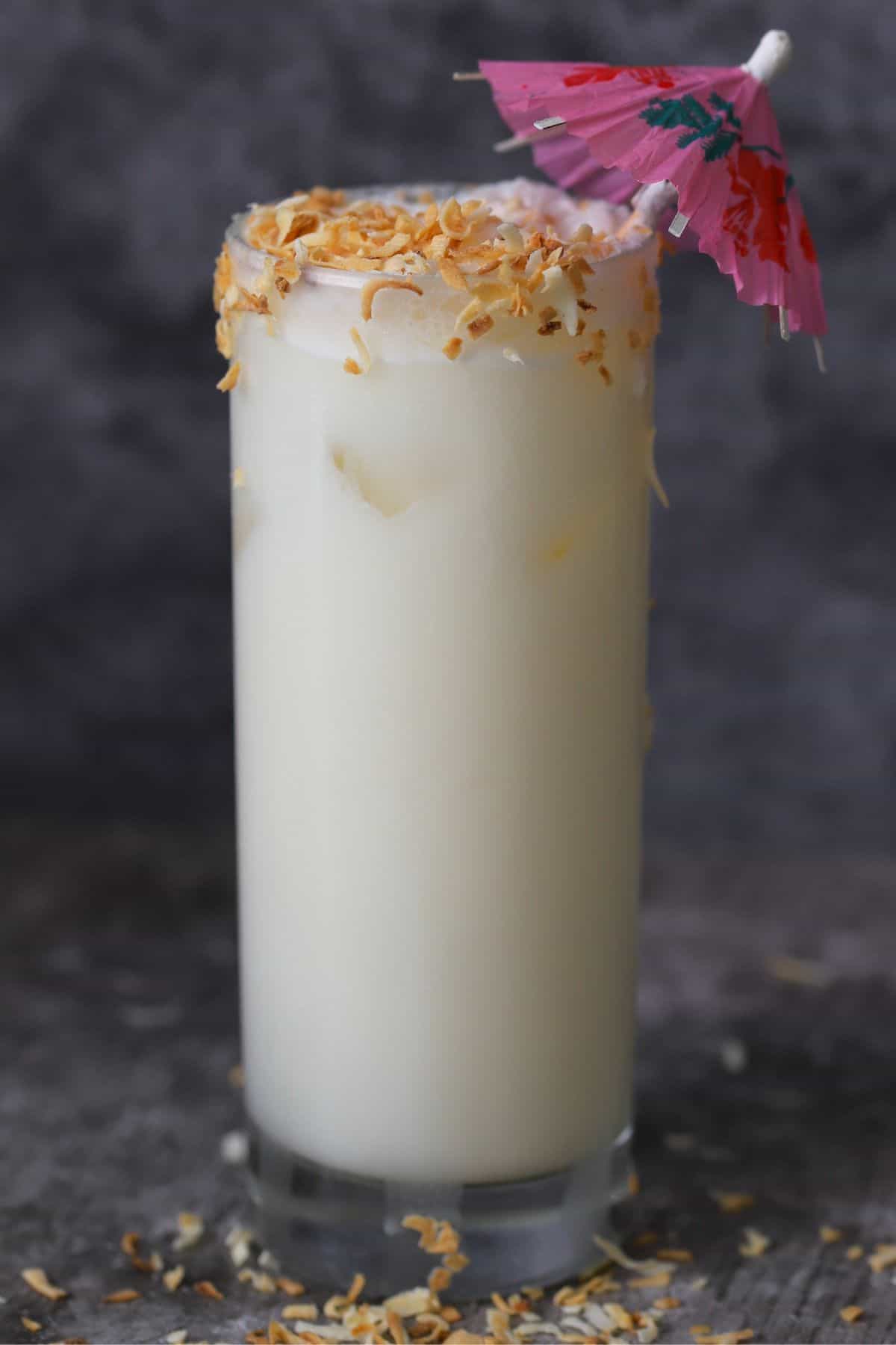 coconut pineapple margarita cocktail garnished with toasted coconut and a cocktail umbrella.