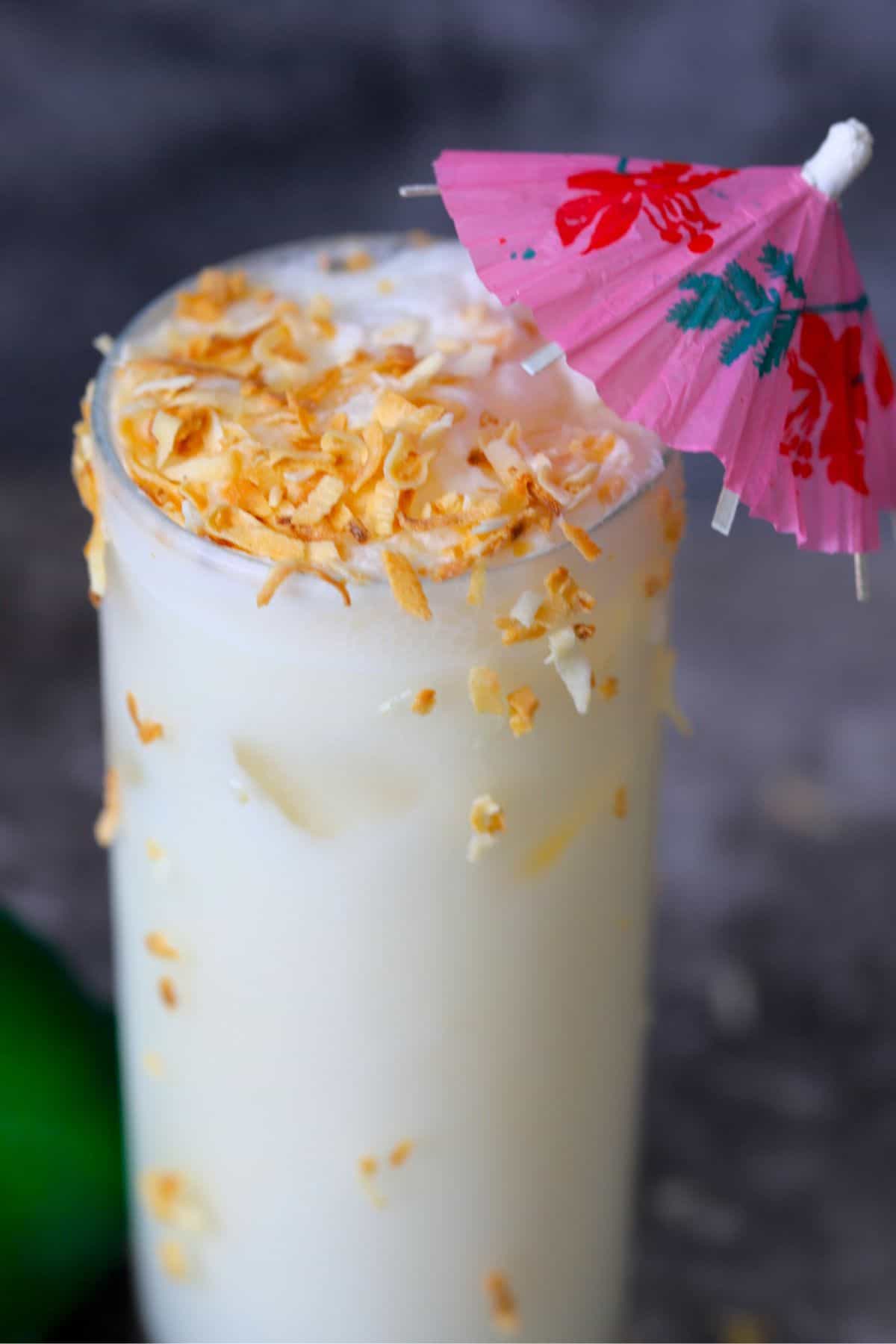 coconut pineapple margarita cocktail garnished with toasted coconut and a cocktail umbrella.