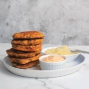 Stacked corned beef fritters next to a small bowl of russian dressing and another small bowl of sauerkraut.