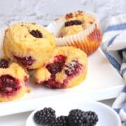 several muffins on a white platter behind a small bowl of blackberries.