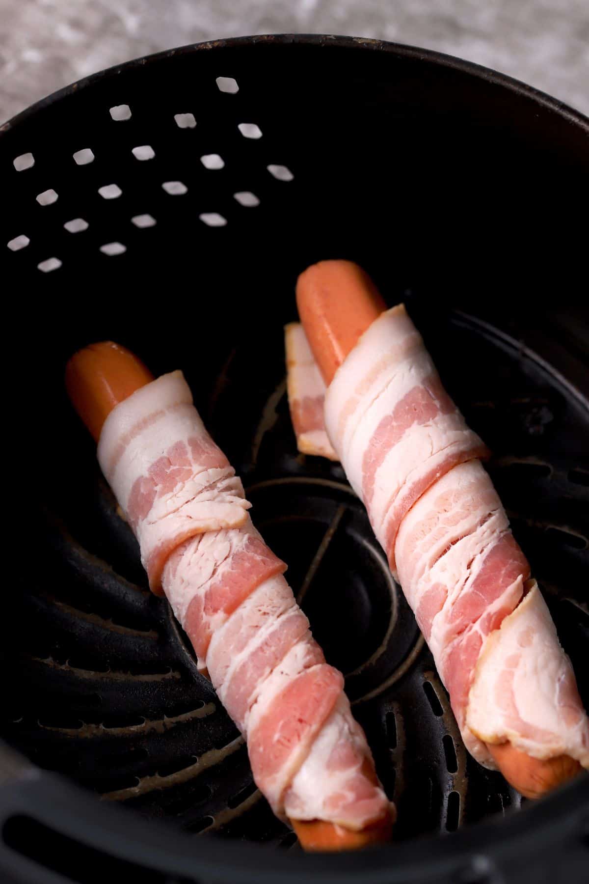 two bacon-wrapped hot dogs in the air fryer basket.