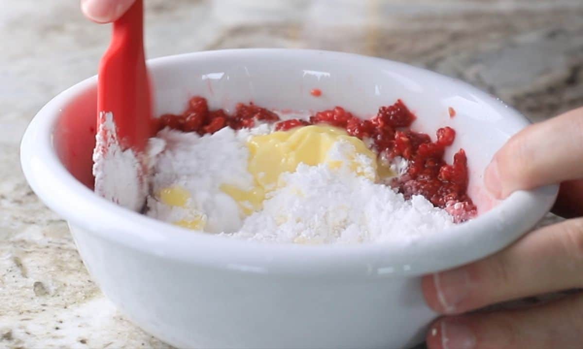 mixing the raspberry icing in a medium white bowl with a red rubber spatula.