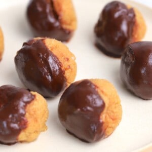 peanut butter bliss balls dipped in chocolate on a white plate.