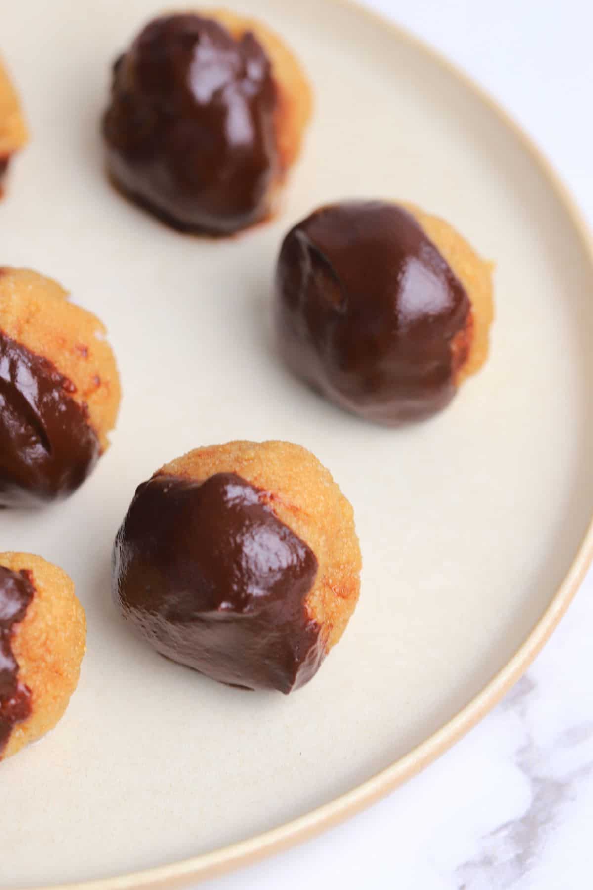 peanut butter bliss balls dipped in chocolate on a white plate.