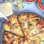Reuben pizza next to a block of swiss cheese, sauerkraut and cans of corned beef.