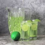two glasses of the sugar free limeade garnished with lime wedges next to the jug and a whole lime.