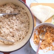 pulled chicken in the dutch oven pot next to a bowl with chicken and taco seasoning.