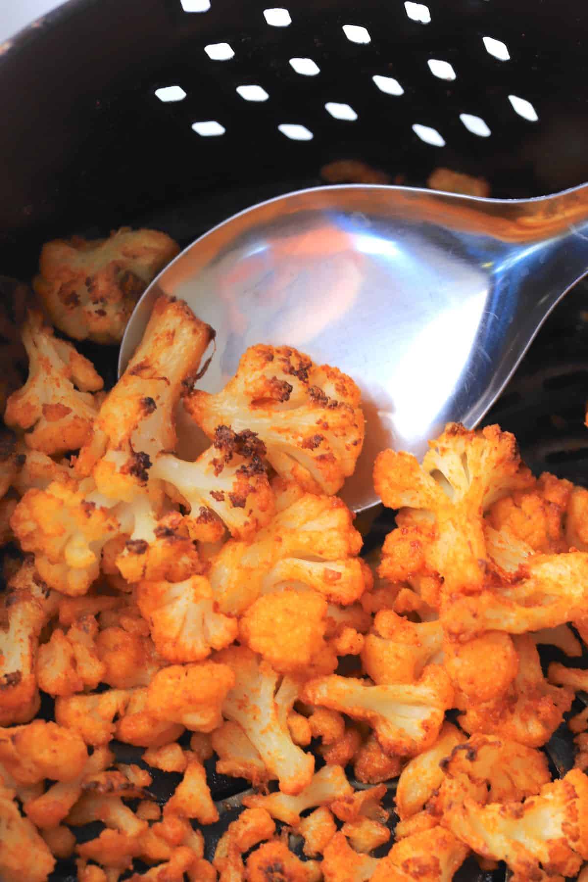 roasted cauliflower in an air fryer basket with a serving spoon.