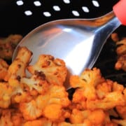 roasted cauliflower in an air fryer basket with a serving spoon.