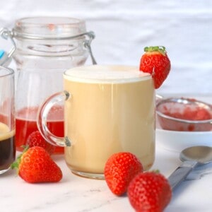 strawberry latte garnished with a strawberry next to a jar, and a strainer.