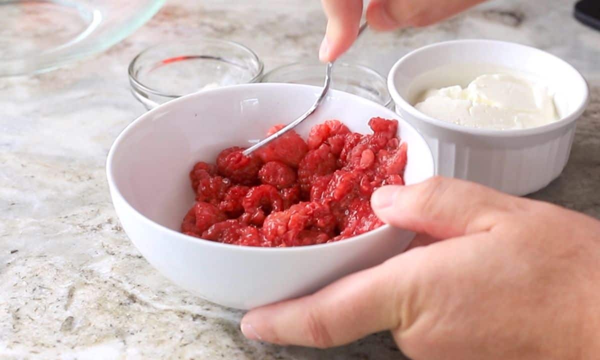 mashing the raspberries in a white bowl.