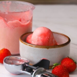 Ninja Creami Strawberry Ice Cream in a bowl next to fresh strawberries and the ninja creami pint.