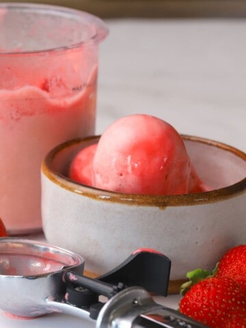 Ninja Creami Strawberry Ice Cream in a bowl next to fresh strawberries and the ninja creami pint.