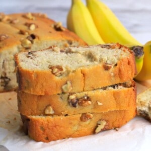 sugar free banana bread slices stacked on top of each other with bananas in the background.