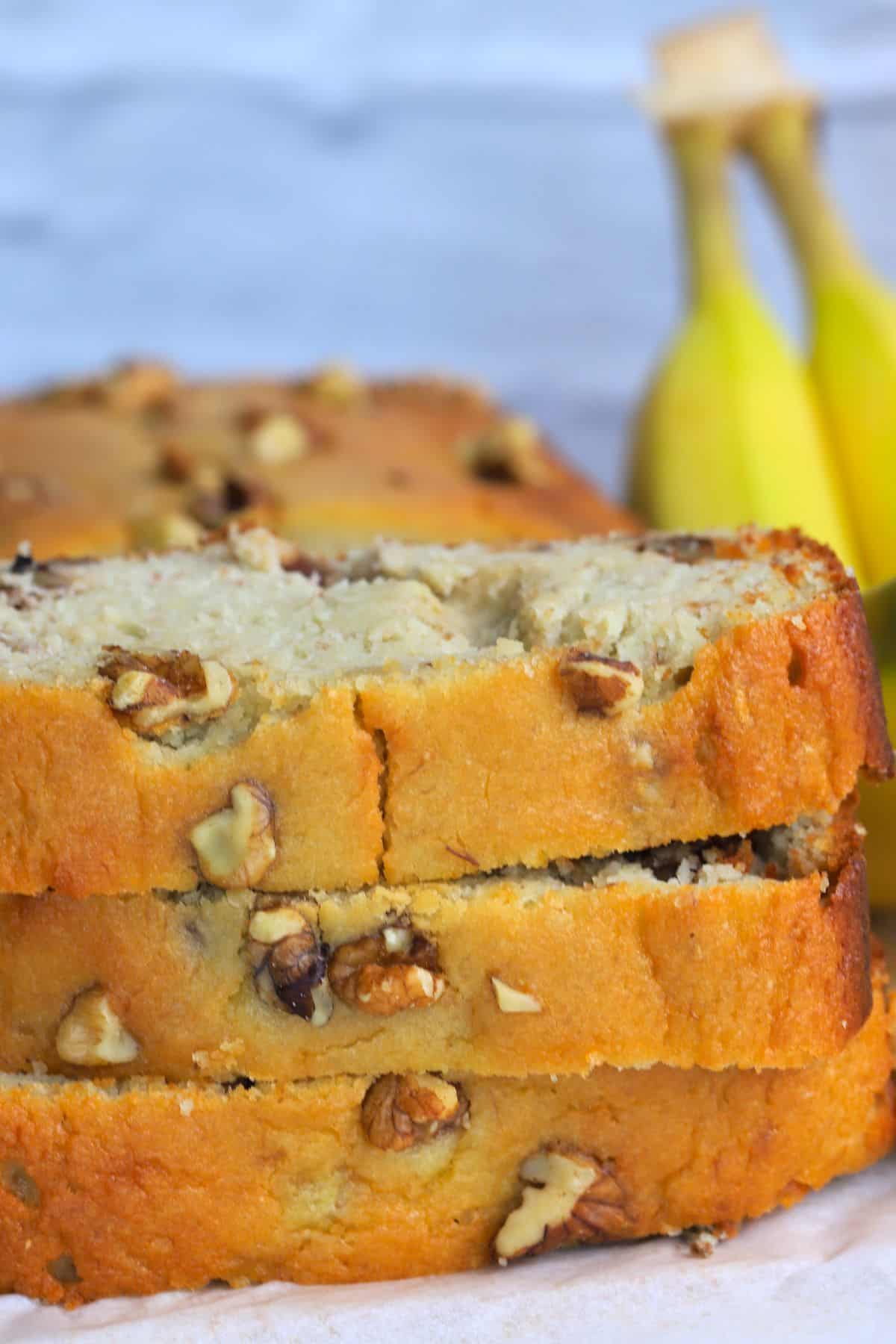 sugar free banana bread slices stacked on top of each other with bananas in the background.