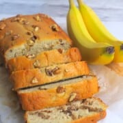 sugar free banana bread loaf cut into slices next to two bananas.