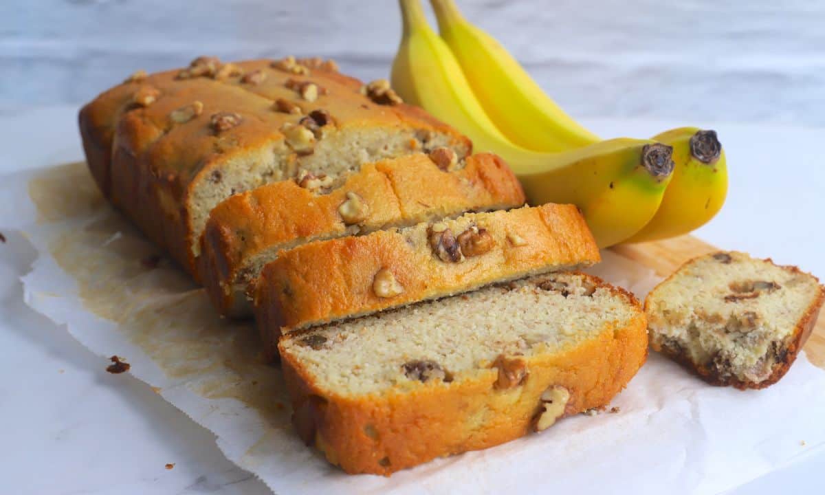 sugar free banana bread loaf cut into slices next to two bananas.